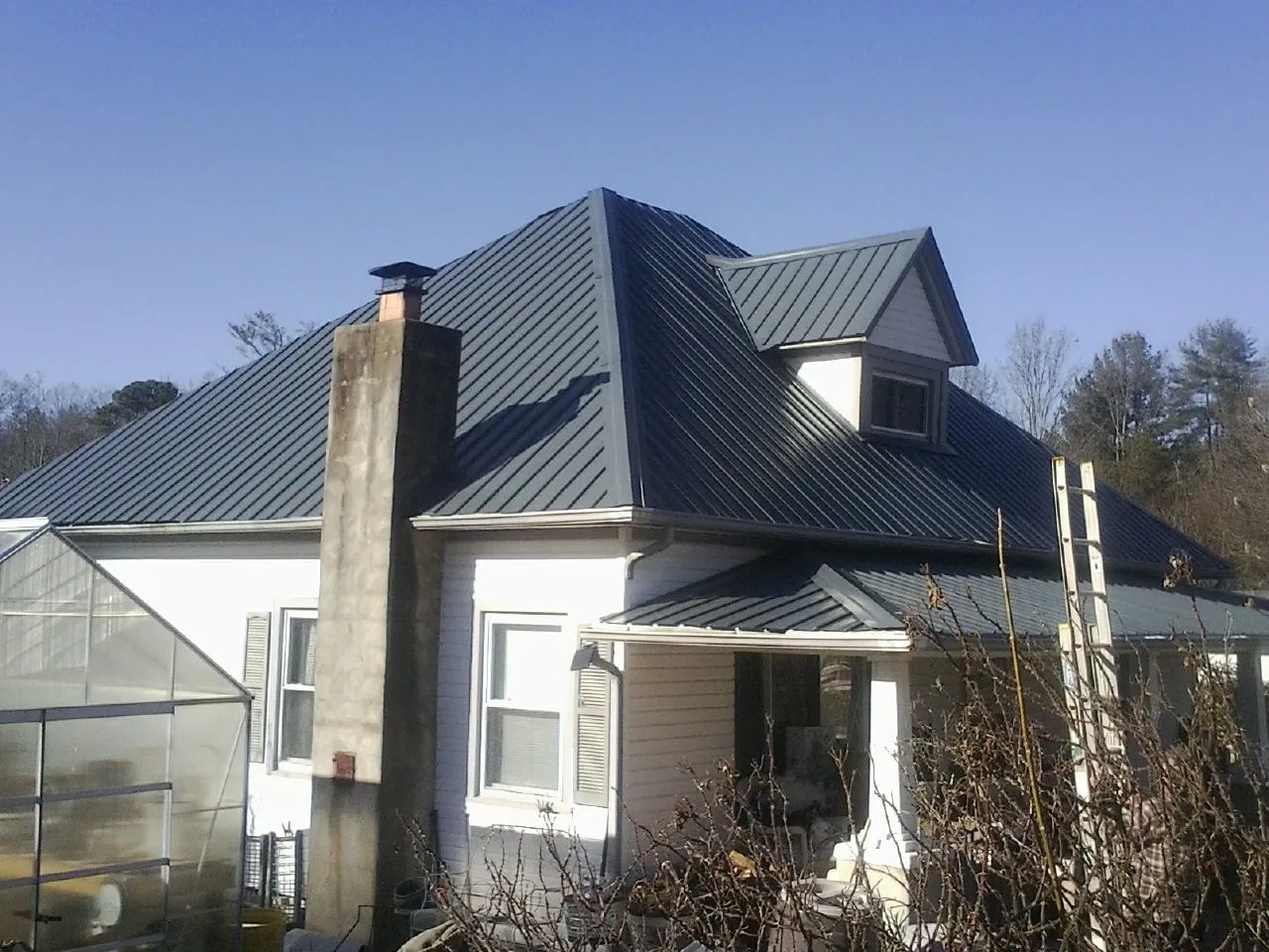 Dark blue standing seam metal roof on a white farmhouse with dormer — Slate & Tile Roof Repair by Roofing Brothers in Waban