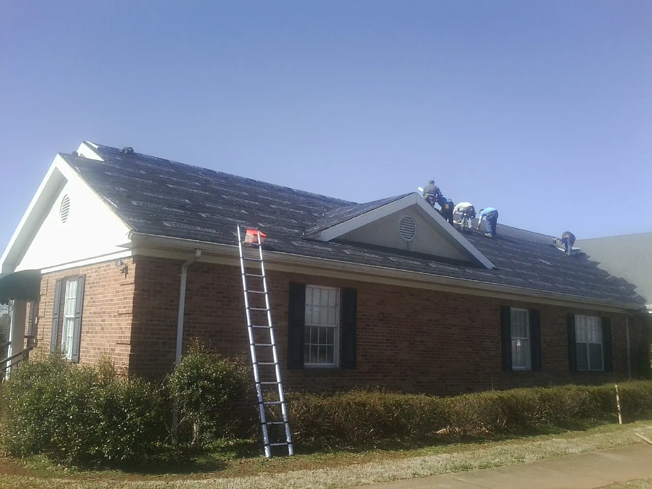 Crew tearing shingles off a brick ranch roof with a ladder set — Metal Roof Repair work by our crew in Waban