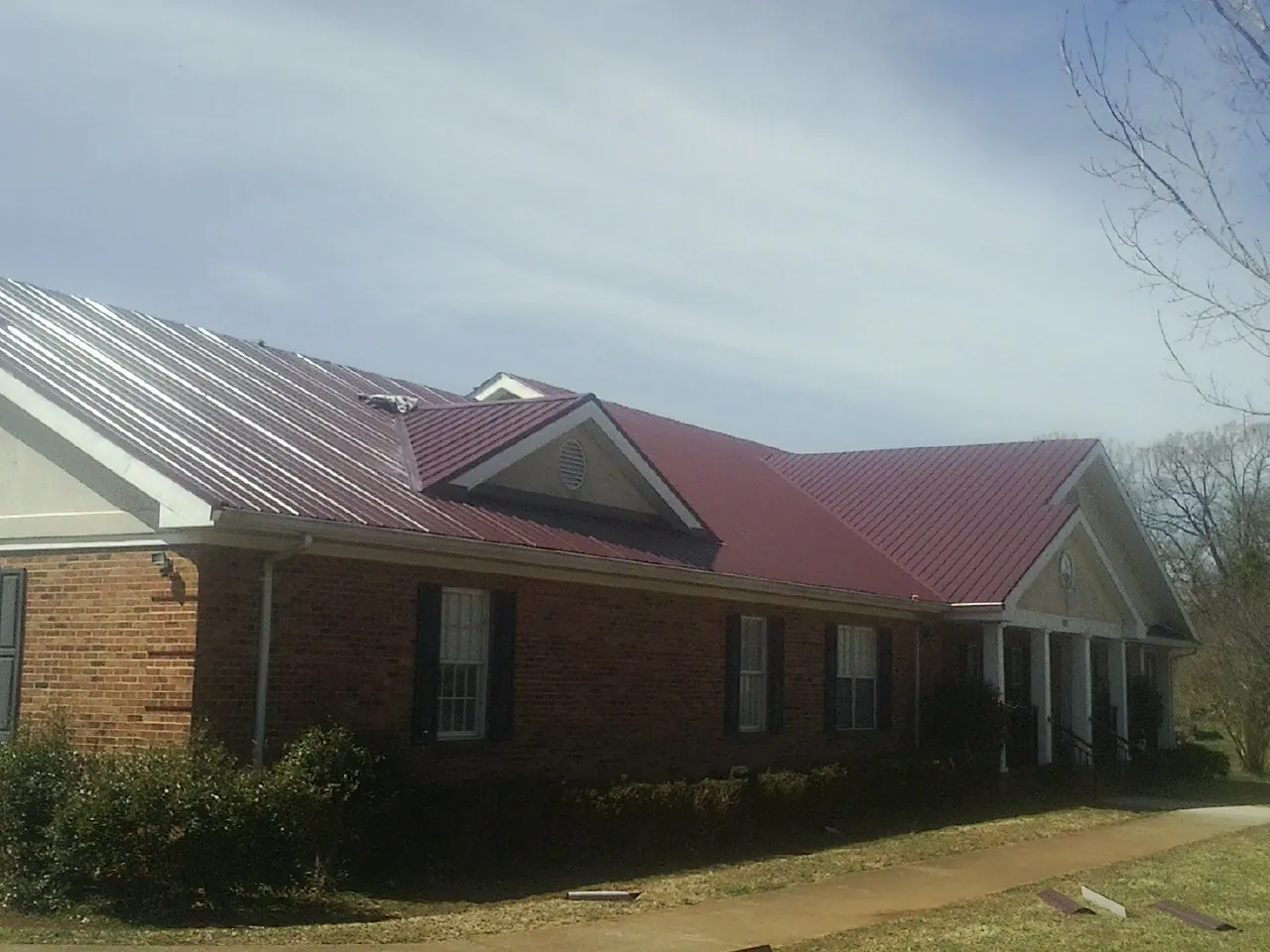 Red metal roof with gabled entries on a long brick building, from a Hail Damage Roof Repair job in Waban