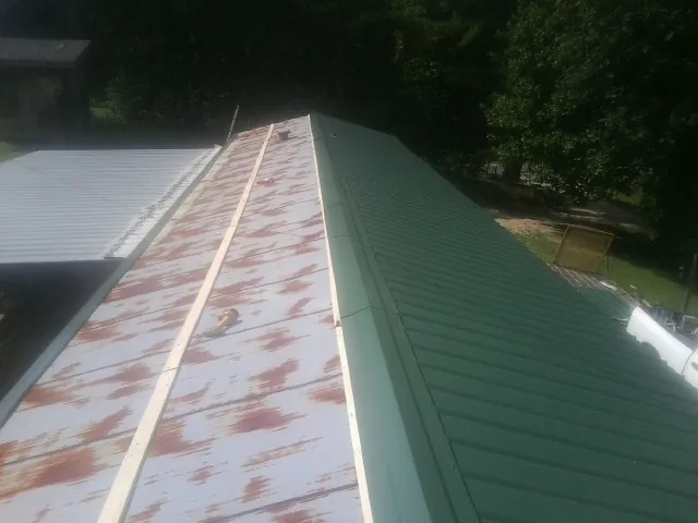 Old rusted panels beside newly installed green metal roofing — Wind Damage Roof Repair by Roofing Brothers in Waban