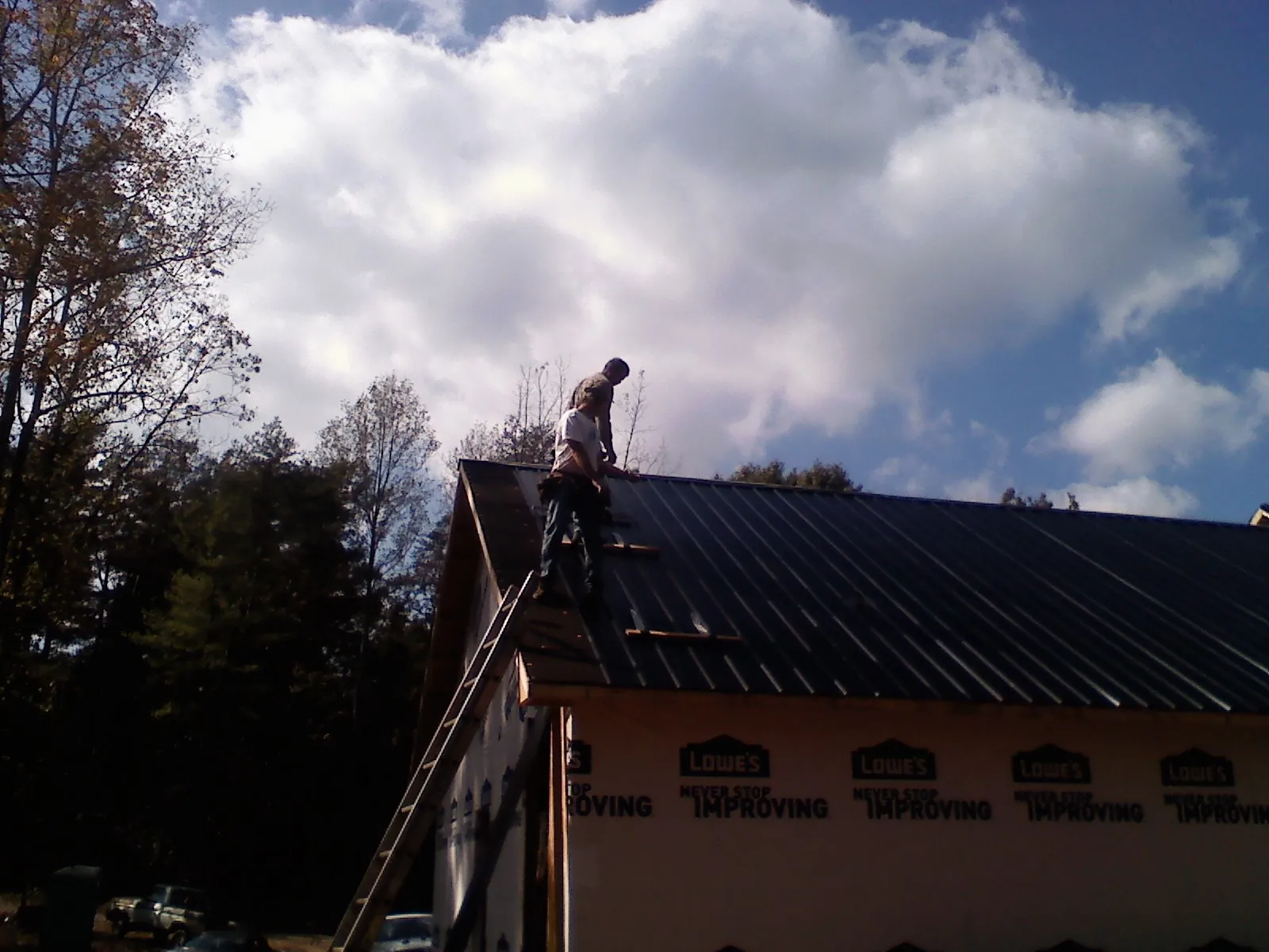 Roofer fastening dark metal panels high against a cloudy sky, from a Roof Inspection job in Waban