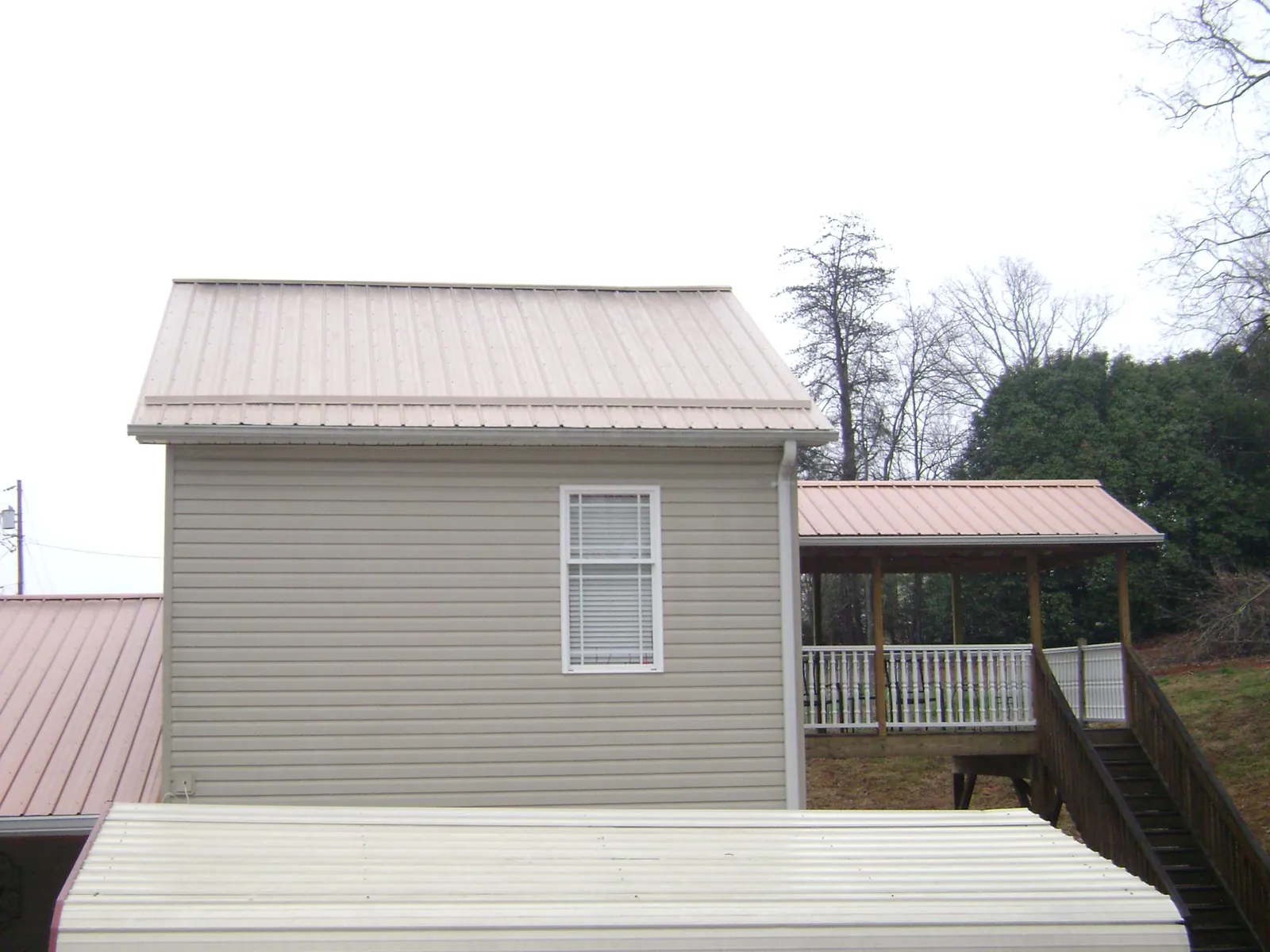 Tan metal roofs on a two story addition and attached porch, from a Roof Replacement job in Waban